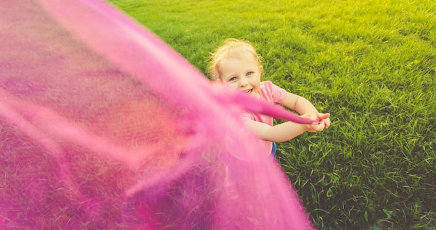 Une petite fille mignonne dans un t-shirt rose et une jupe en jean court autour du terrain et attrape des papillons. Mode de vie.