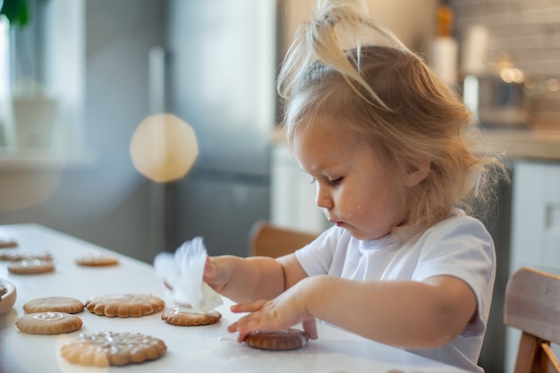 La petite fille mignonne décore le pain d'épice avec la préparation de glaçage de sucre pour le concept de Noël