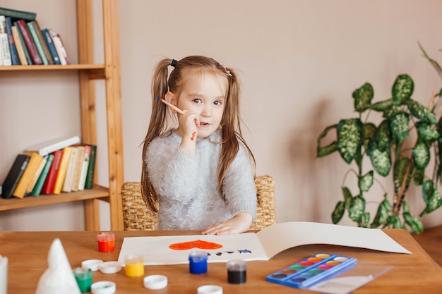 La petite fille mignonne dessine avec des peintures à la table dans le salon