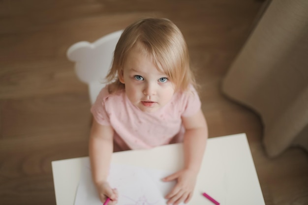 Une petite fille mignonne dessine à la table avec des crayons