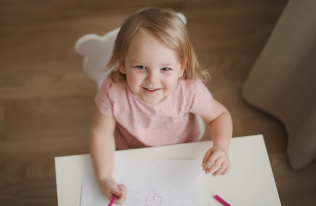 Une petite fille mignonne dessine à la table avec des crayons