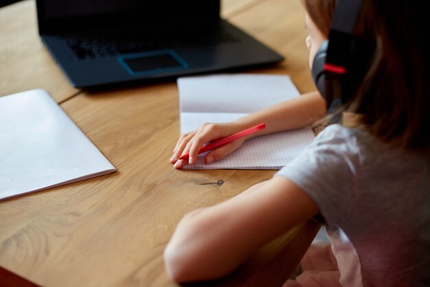 Petite fille mignonne avec des écouteurs utilisant un ordinateur portable pour étudier à la maison