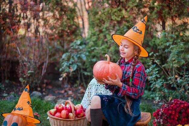 Une petite fille mignonne embrasse une citrouille dans le jardin d'automne. Célébrer la récolte d'automne.