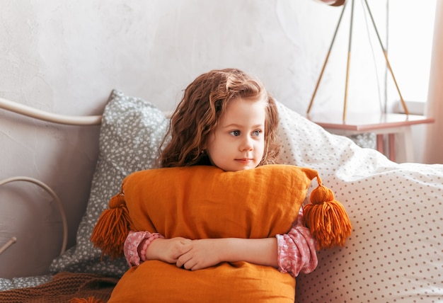 Petite fille mignonne embrasse l'oreiller sur le lit dans la chambre des enfants