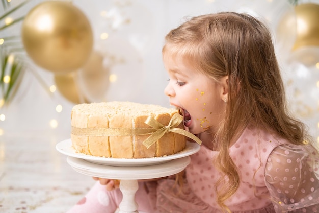 Petite fille mignonne d'enfant mangeant le gâteau d'anniversaire sans main et célébrant l'anniversaire