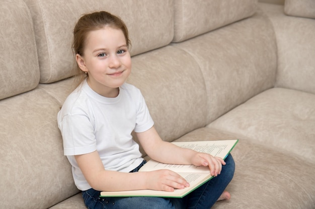 Petite fille mignonne est assise dans une pièce sur un canapé de style turc tient un livre sur ses genoux et sourit