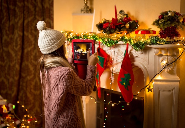 Petite fille mignonne faisant la photo de la cheminée de Noël décorée sur la tablette numérique