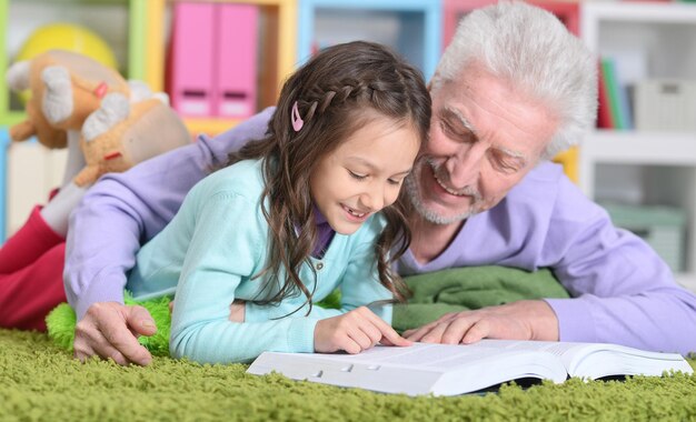 Petite fille mignonne avec grand-père lisant un livre