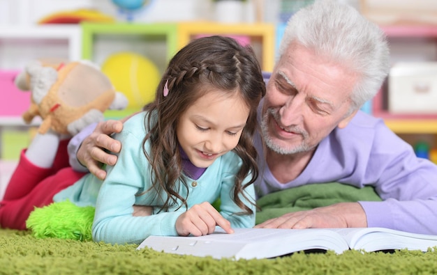 Petite fille mignonne avec grand-père lisant un livre