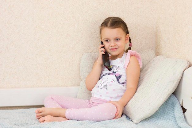 Petite fille mignonne à l'intérieur de la maison parlant avec un téléphone portable et souriant