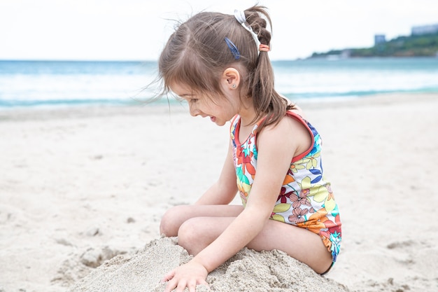 Petite fille mignonne jouant dans le sable sur la plage au bord de la mer. Animations et loisirs d'été.