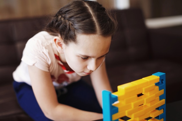 La petite fille mignonne joue à un jeu de société de briques en plastique jaunes