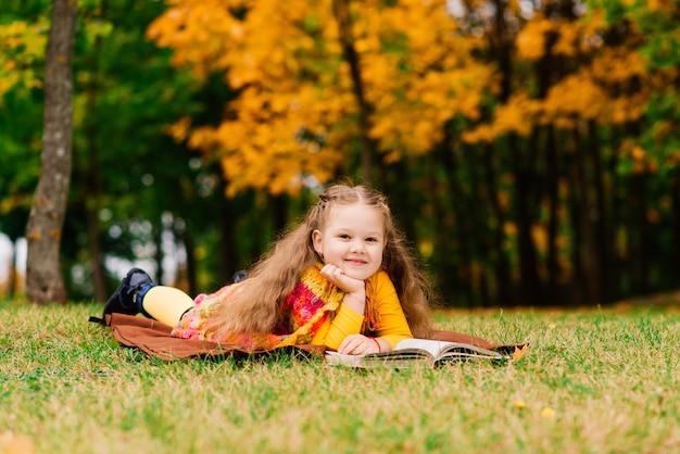 Petite fille mignonne lisant un livre en parc d'automne