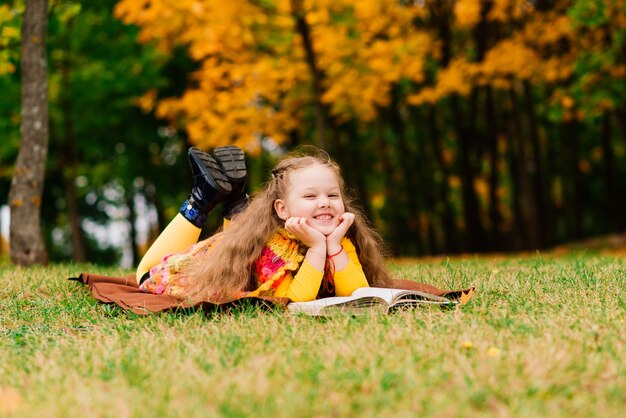 Petite fille mignonne lisant un livre en parc d'automne