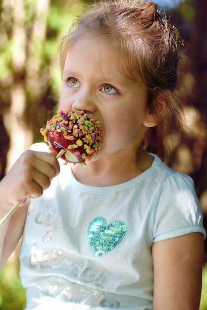 La petite fille mignonne mange la pomme de sucrerie