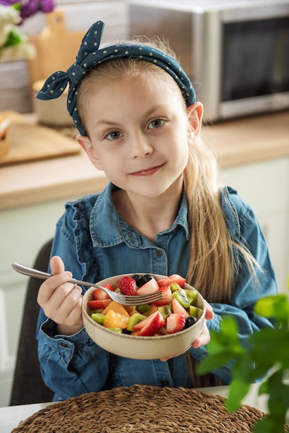 La petite fille mignonne mange la salade de fruit