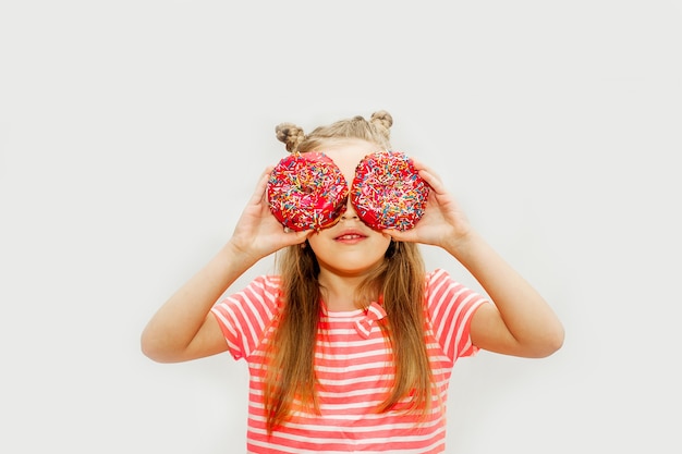 Petite fille mignonne mangeant des beignets sucrés sur un fond clair.