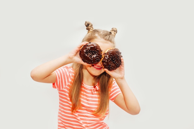 Petite fille mignonne mangeant des beignets sucrés sur un fond clair.