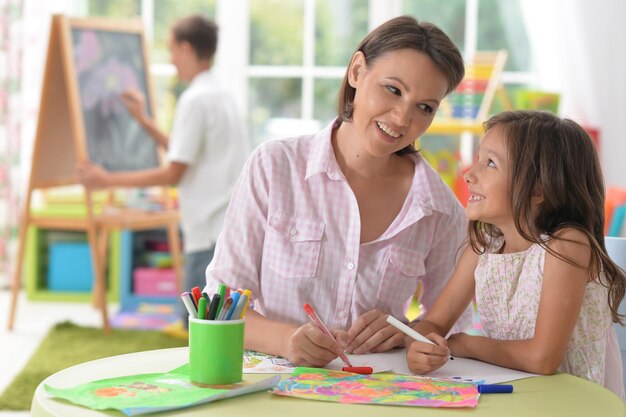 Petite fille mignonne avec la mère dessinant à la maison