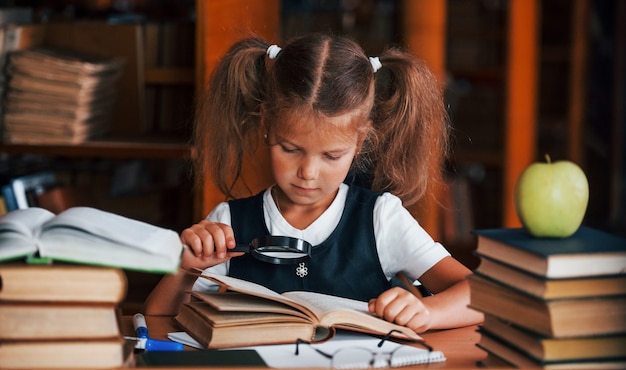 La petite fille mignonne avec des nattes est dans la bibliothèque