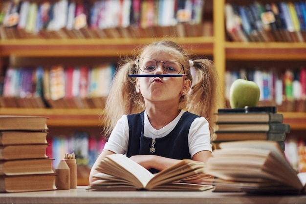 La petite fille mignonne avec des nattes est dans la bibliothèque