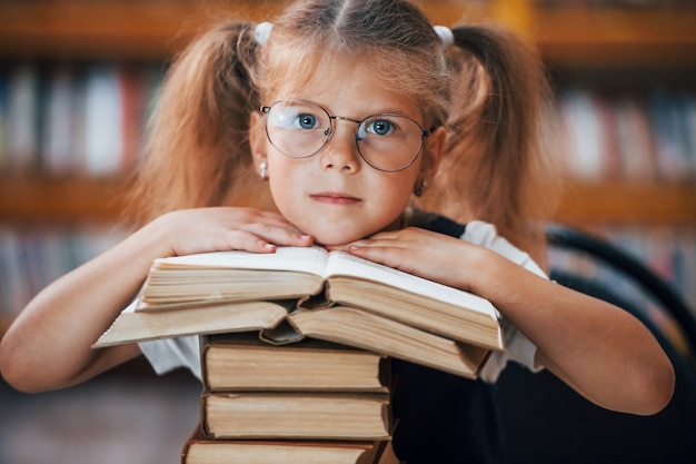 La petite fille mignonne avec des nattes est dans la bibliothèque