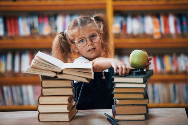 La petite fille mignonne avec des nattes est dans la bibliothèque