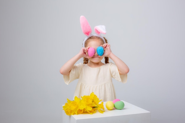 Petite fille mignonne avec des oreilles de lapin sur un fond blanc avec un panier des oeufs et des fleurs de pâques