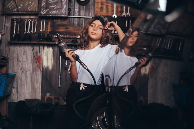 Petite fille mignonne pose avec une perceuse pneumatique pour photographe à l'atelier de service automobile.