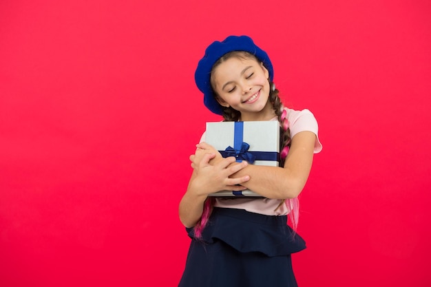 Petite fille mignonne a reçu un cadeau de vacances Meilleurs cadeaux de Noël Enfant excité à l'idée de déballer son cadeau Petite fille tenant une boîte-cadeau avec ruban sur fond rouge Cadeau de Noël pour fille