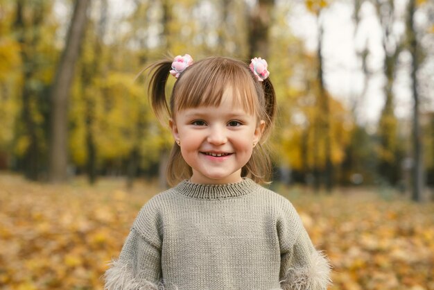 La petite fille mignonne rit dans la forêt d'automne parmi les feuilles jaunes