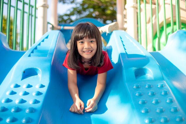 Petite fille mignonne s'amusant sur une aire de jeux à l'extérieur en été