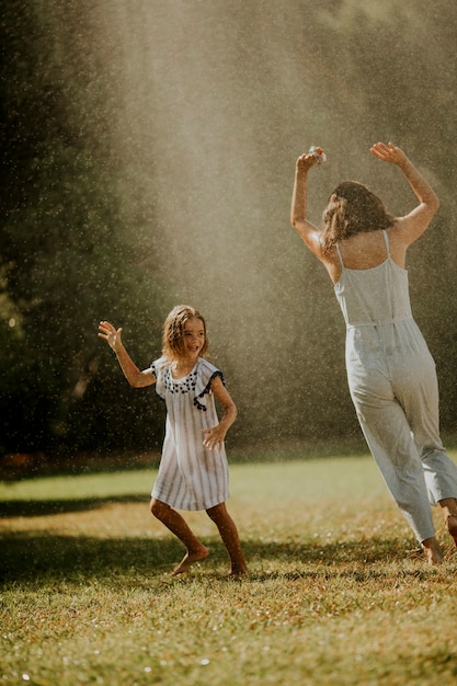 Petite fille mignonne s'amusant avec de l'eau sous l'arroseur d'irrigation avec sa mère