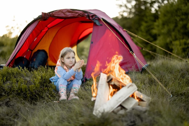 Petite fille mignonne s'asseoir seule et profiter d'un feu de camp au camping