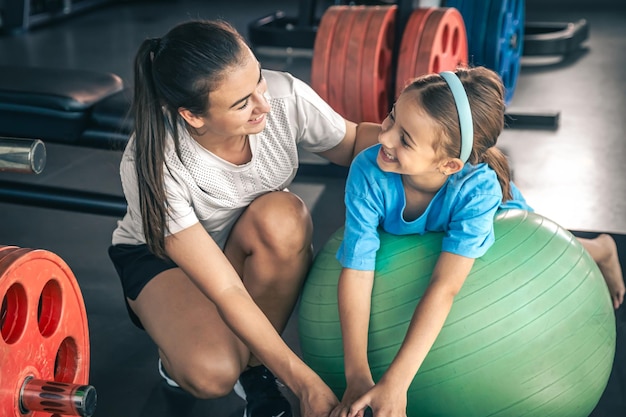 Une petite fille mignonne s'étire sur une balle de pilates avec sa mère au gymnase.