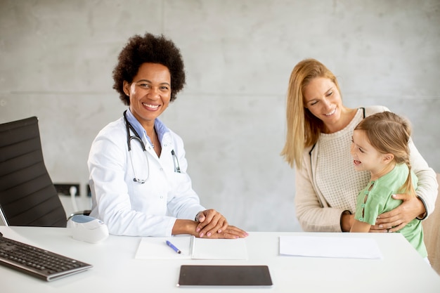 Petite fille mignonne avec sa mère à l'examen pédiatrique par une femme médecin afro-américaine