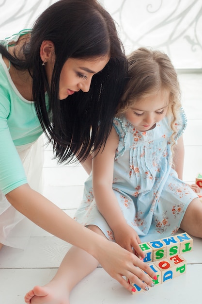 Petite fille mignonne et sa mère jouant et éduquant avec des cubes abc à l'intérieur. Jeune jolie mère et sa fille jouant des blocs.