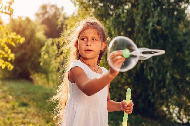 Petite fille mignonne, soufflant des bulles dans le parc du printemps. Enfant s'amusant à jouer à des jeux à l'extérieur.