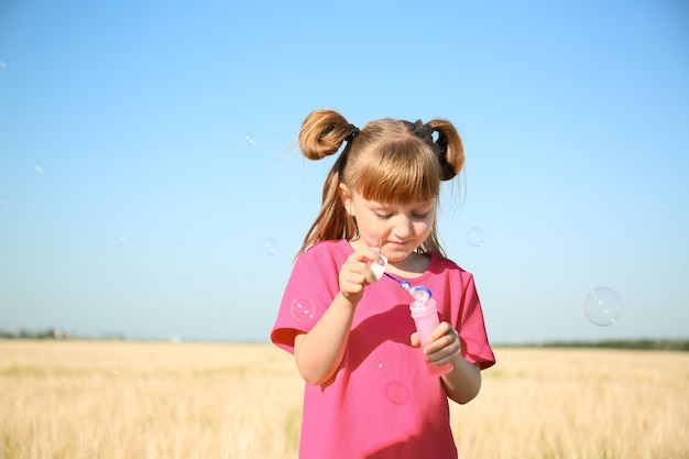 Petite fille mignonne soufflant des bulles de savon dans le domaine le jour ensoleillé