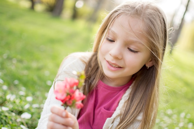 Petite fille mignonne souriante sur le pré au printemps tenant une fleur et le regardant.