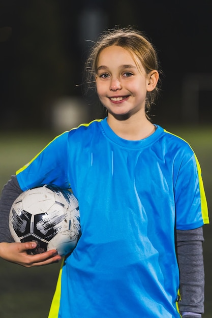 Photo petite fille mignonne souriante tenant une balle dans la main et posant un tir vertical moyen