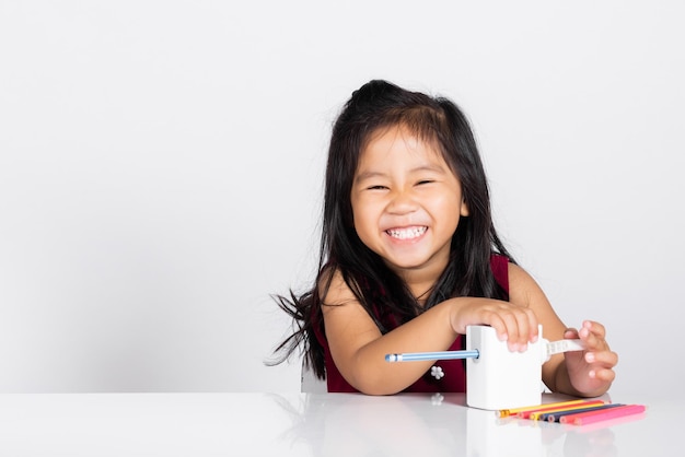 Petite fille mignonne sourit à l'aide d'un taille-crayon tout en faisant ses devoirs