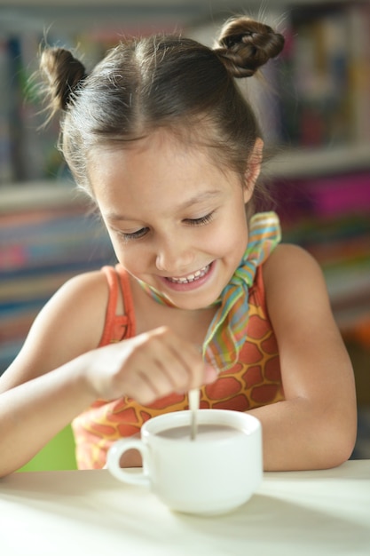 Petite fille mignonne avec une tasse de cacao sur la table