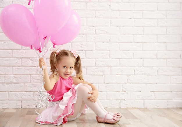 Petite fille mignonne tenant des ballons de fête sur fond de mur de briques