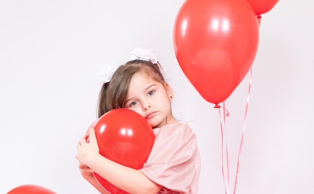 Petite fille mignonne tenant un groupe de ballons rouges en forme de coeur