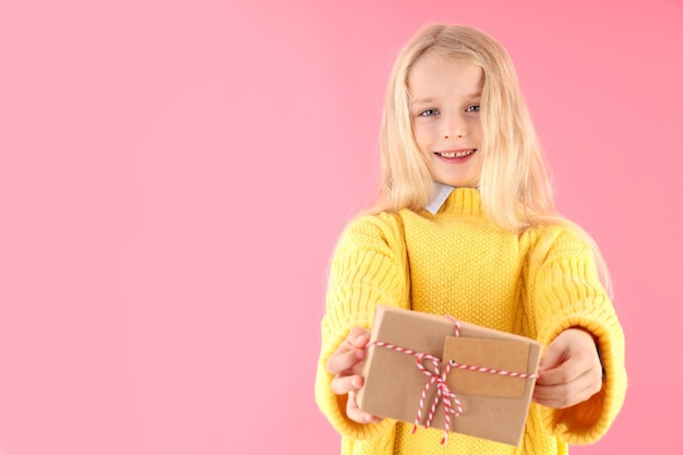 La petite fille mignonne tient la boîte-cadeau sur le fond rose