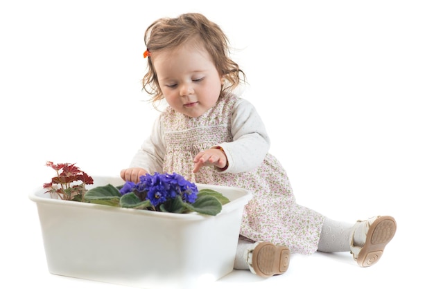 La petite fille mignonne verse des fleurs dans un pot sur un fond blanc