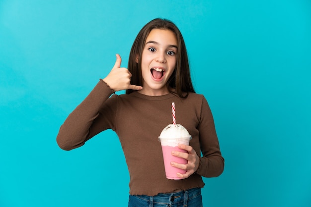 Petite fille avec milk-shake aux fraises isolé sur fond bleu faisant le geste du téléphone. Rappelez-moi signe