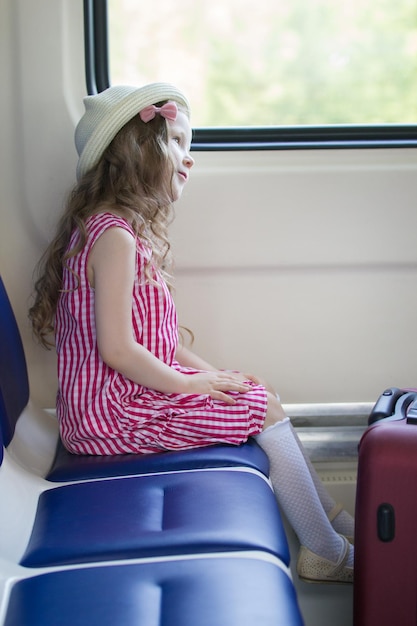Petite fille à la mode assise sur un fauteuil près de la fenêtre dans le train