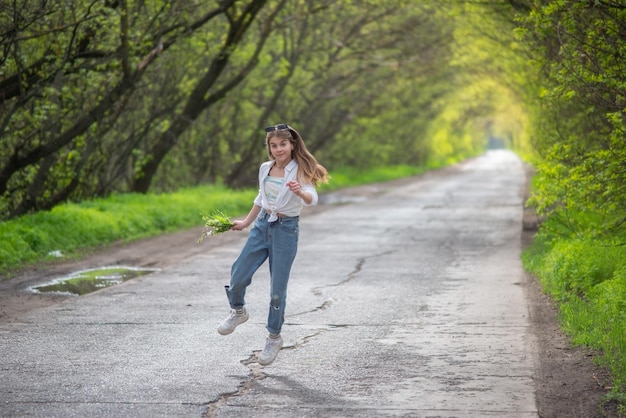 Petite fille à la mode debout marchant sur la route dans le contexte d'une arche d'arbres ramifiés verts